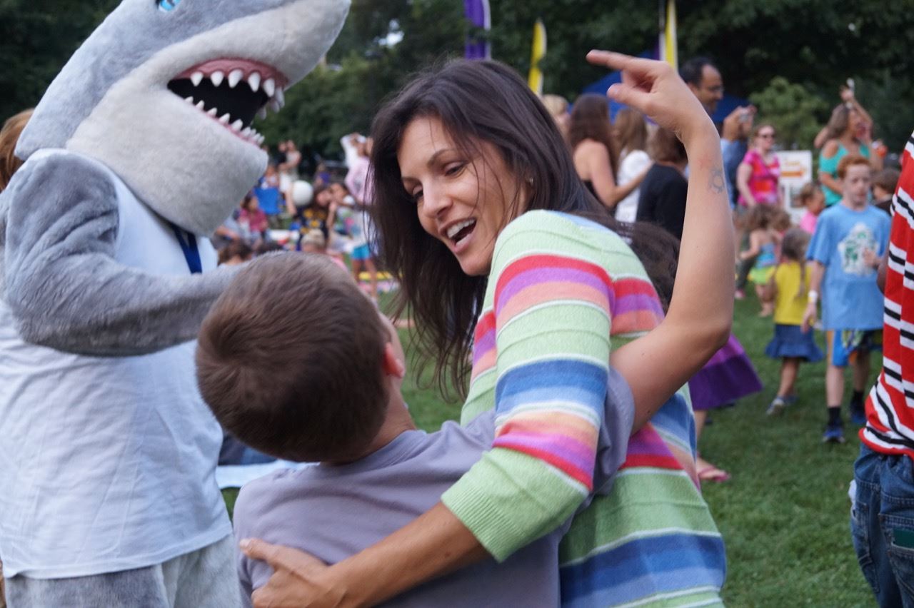 Woman hugs a little boy standing next to the shark mascot.